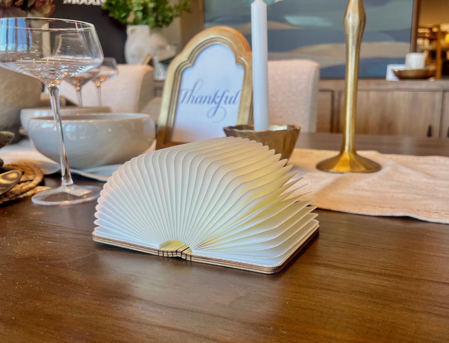 Foldable i lumi book lighting up on a wooden dining table with a 'Thankful' card in the background